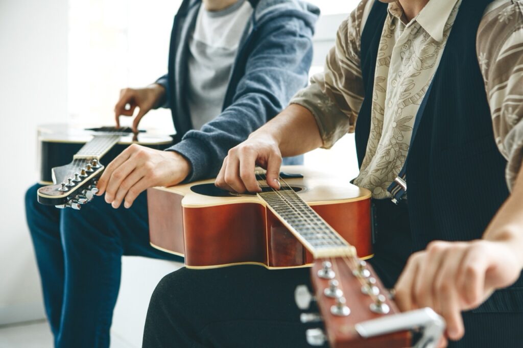 Two men sitting down tuning a guitar.
